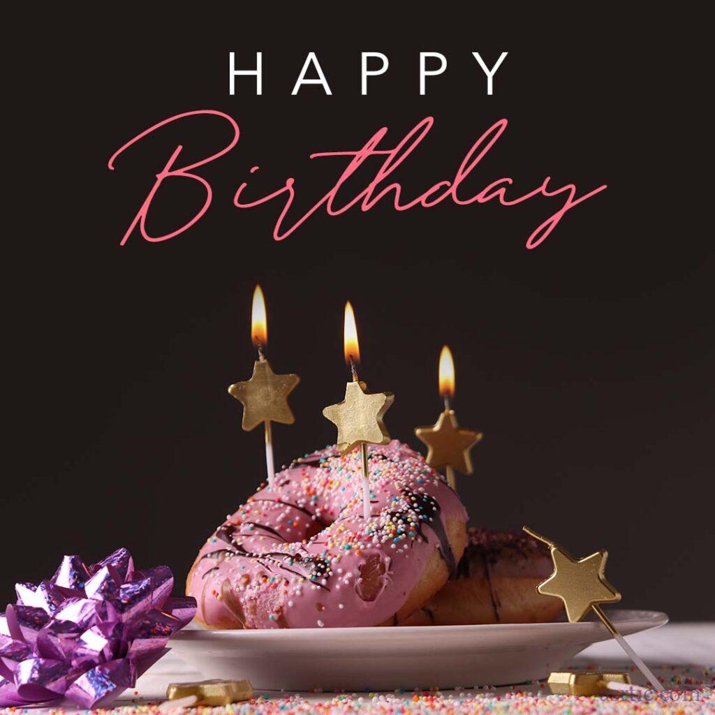 A plate of colourful pastel pink doughnuts with sprinkles, golden star-shaped candles and birthday wishes for dearest buddies